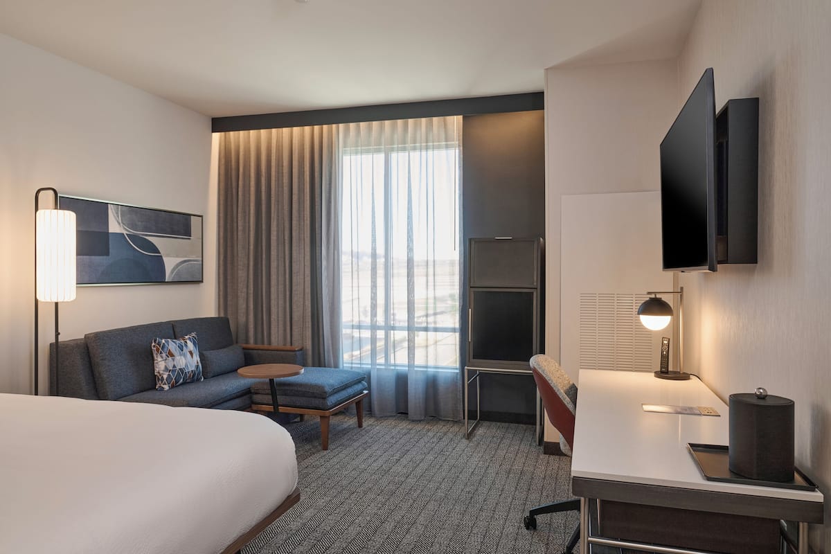 A hotel room with a bed, a sofa, a desk, a TV, and a window with curtains.