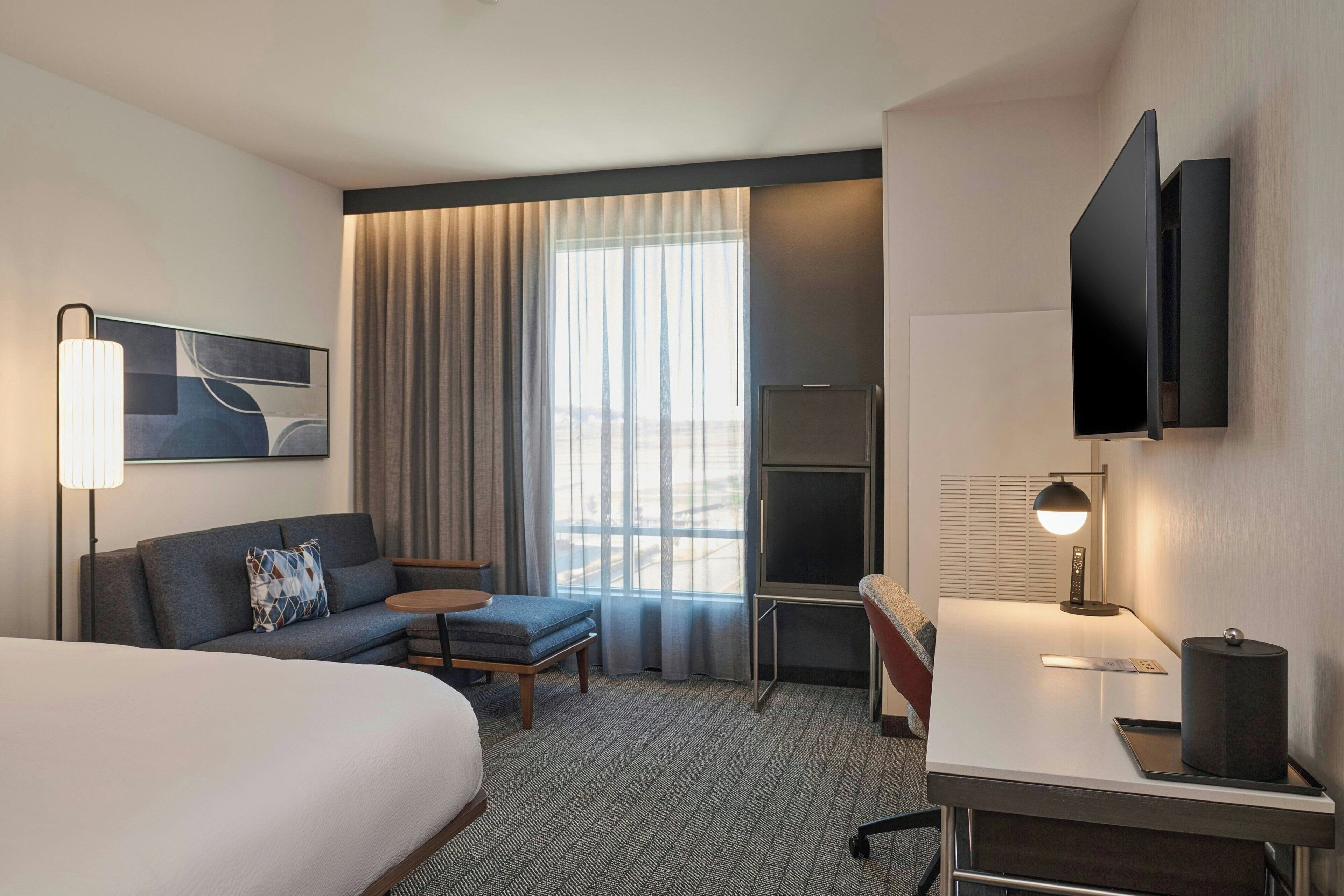 Une chambre d’hôtel équipée d’un lit, d’un bureau, d’une chaise, d’un canapé, d’une télévision et d’une fenêtre avec des rideaux.