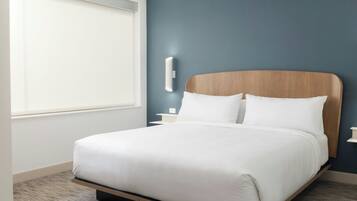 Una habitación de hotel moderna con una cama grande, una mesita de noche, una lámpara de pared y una ventana con persianas.