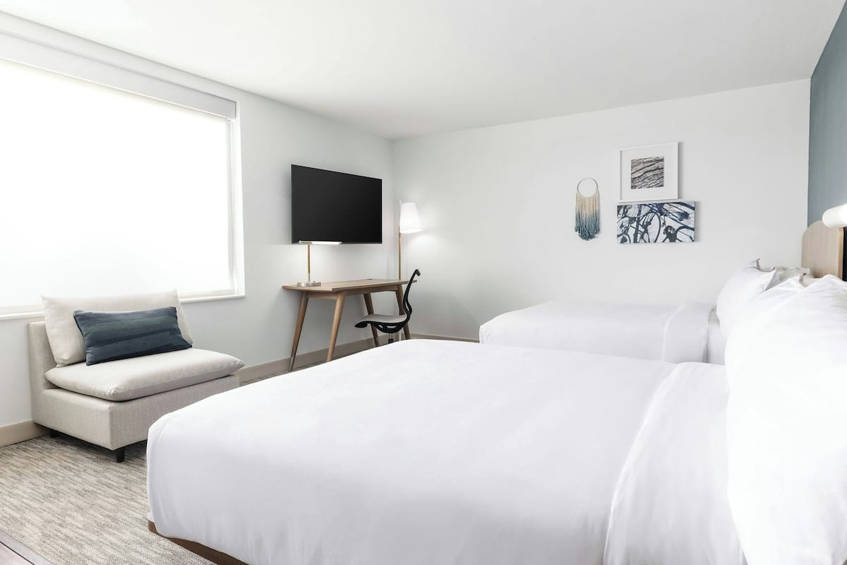Ein Hotelzimmer mit zwei Betten, einem Sofa, einem Fernseher und Kunstwerken an der Wand.