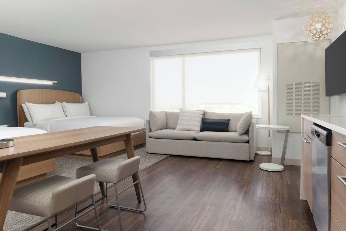 Ein modernes Hotelzimmer mit Bett, Sofa, Esstisch, Stühlen und einer Küchenzeile.