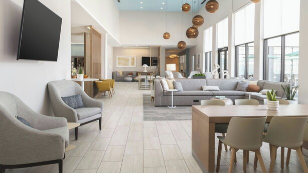 Un vaste espace de vie comprenant un grand canapé, une table à manger et plusieurs chaises. Des luminaires suspendus et un téléviseur à écran plat fixé au mur complètent l’ensemble.