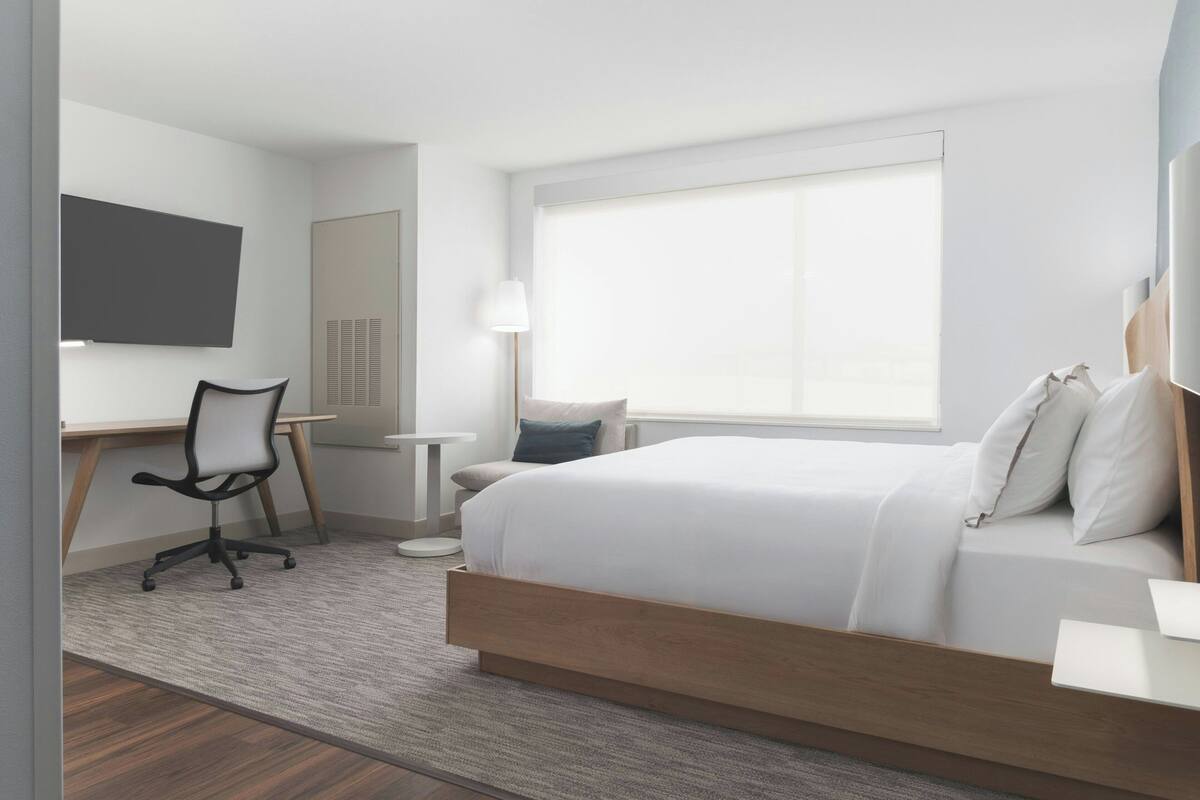 Ein modernes Hotelzimmer mit Bett, Schreibtisch, Stuhl und einem großen Fenster.