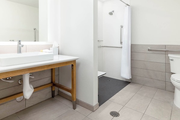 Une salle de bain moderne équipée d’un lavabo, d’un miroir, d’une douche et de toilettes.