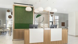 Un espace d’accueil moderne, avec un comptoir en bois, un jardin vertical verdoyant et une grande fenêtre laissant entrer la lumière naturelle.