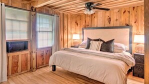 Een slaapkamer met houten lambrisering, een bed, twee bedlampen en een plafondventilator.