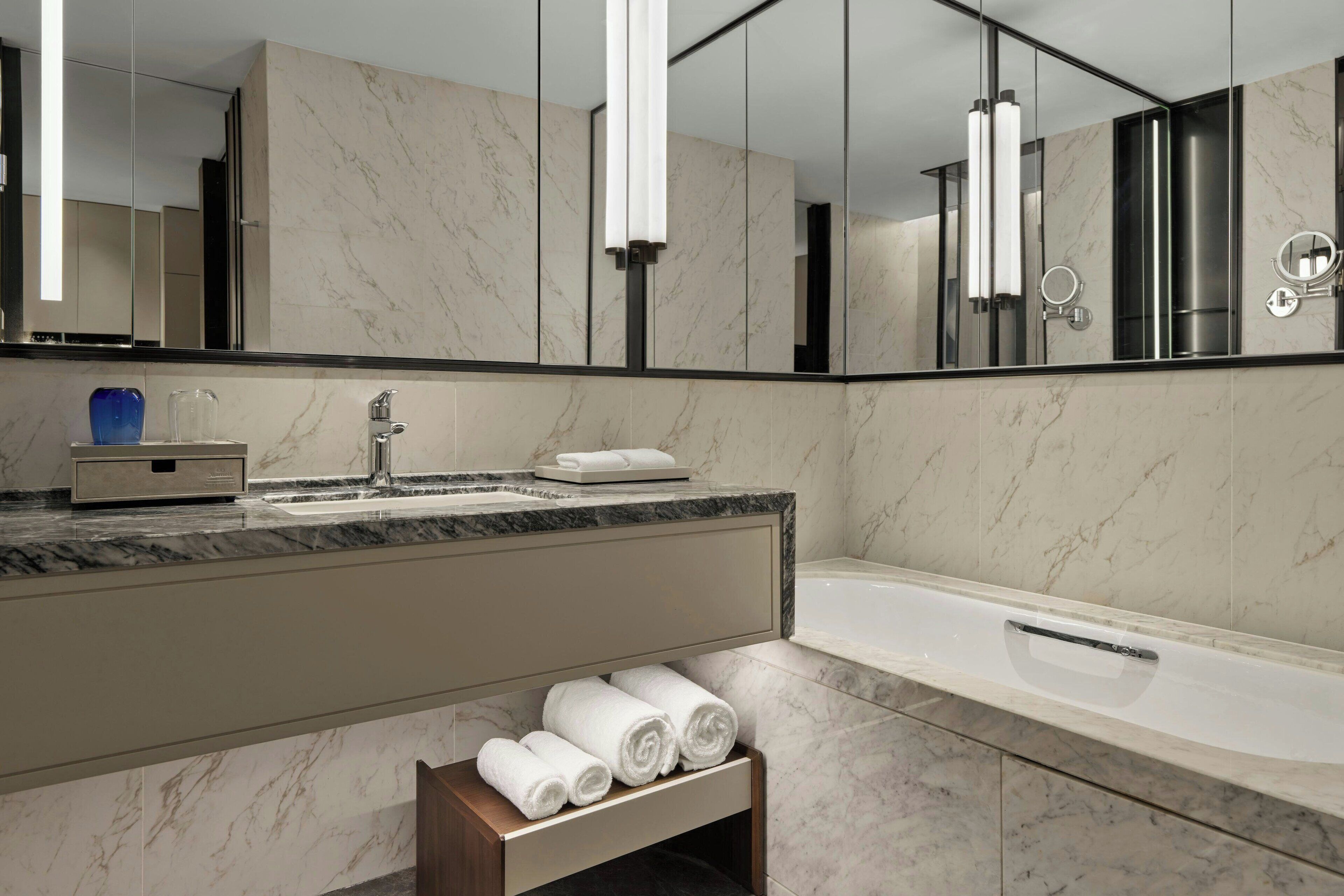 Un baño moderno con un lavabo de mármol, un espejo grande y una bañera.