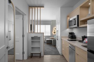 A modern kitchen with a microwave, refrigerator, and coffee maker. There is a small dining area with a table and chairs.