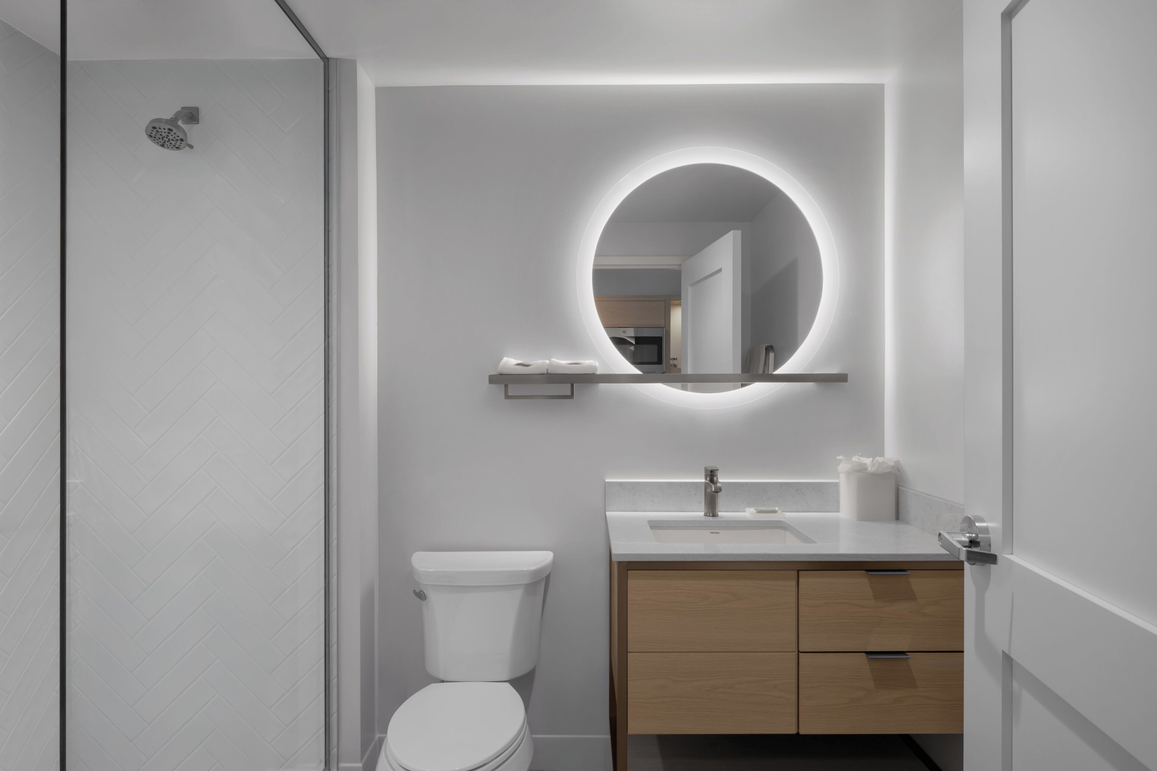 A modern bathroom with a toilet, sink, and mirror with a circular light.