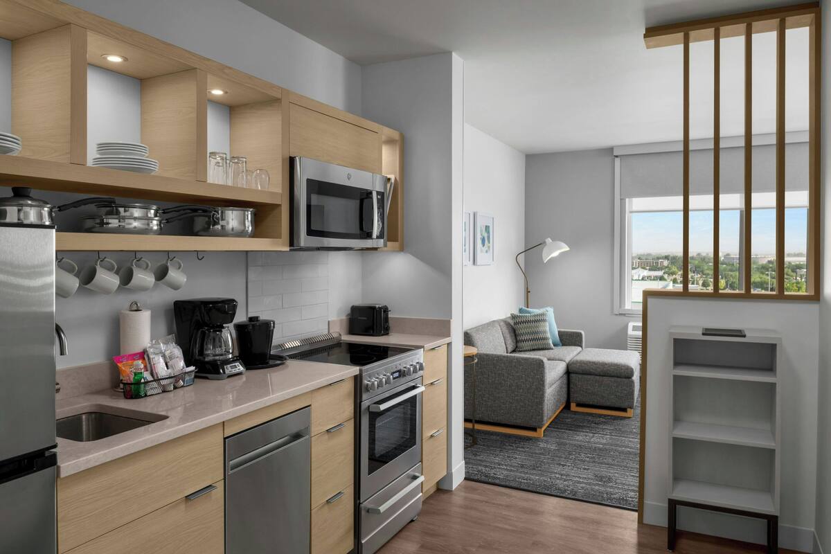 Une cuisine moderne dotée d’appareils électroménagers en acier inoxydable, de meubles en bois et d’un canapé gris dans le salon attenant.