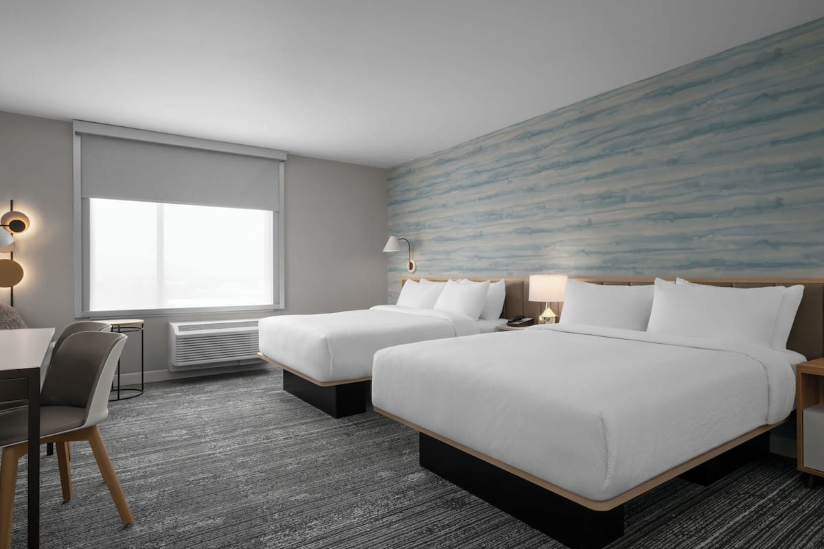 Une chambre d’hôtel avec deux lits, un bureau, une chaise et une grande fenêtre.
