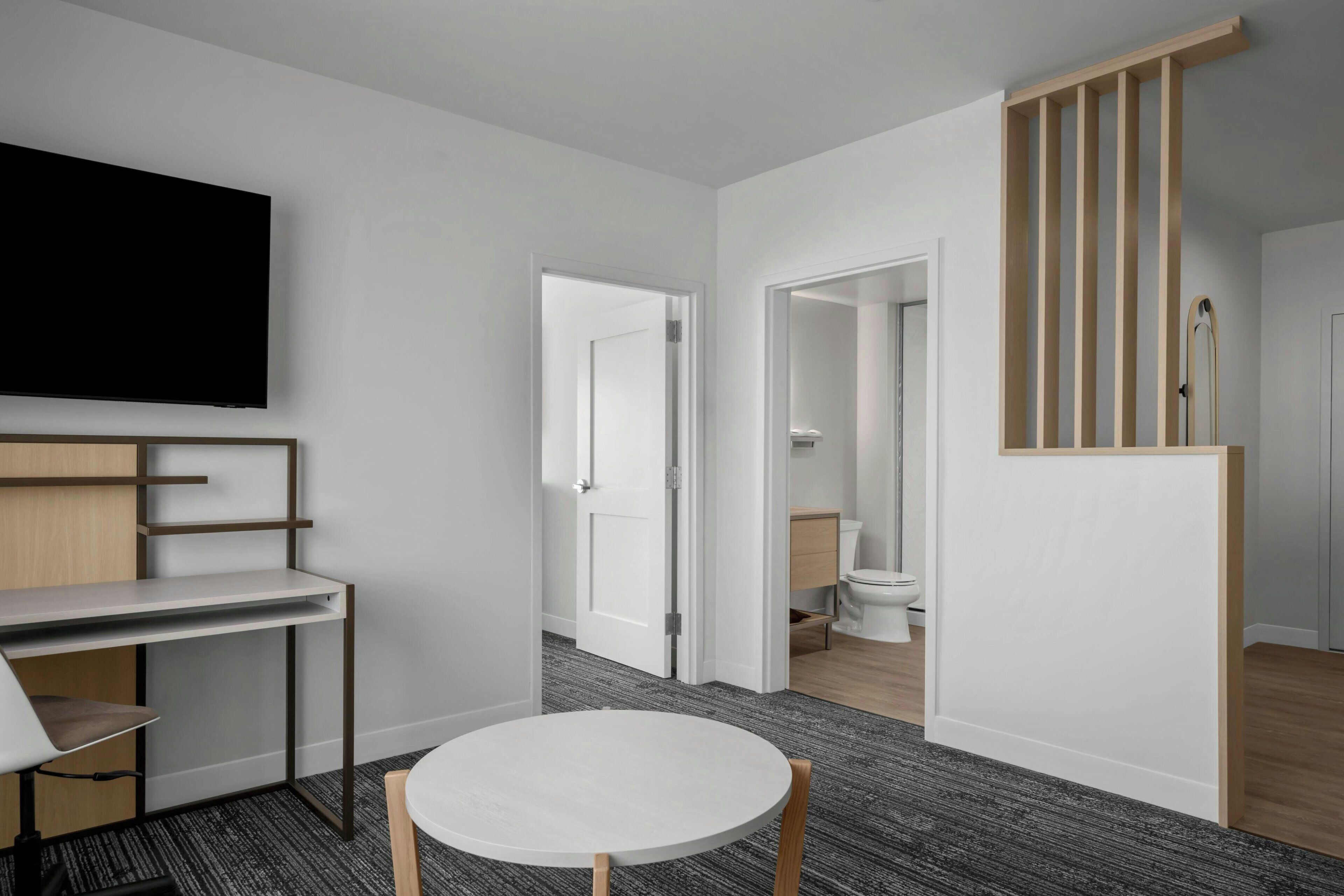 Una habitación de hotel moderna con una televisión de pantalla plana, un escritorio con silla, una mesa redonda y una escalera con barandillas de madera.