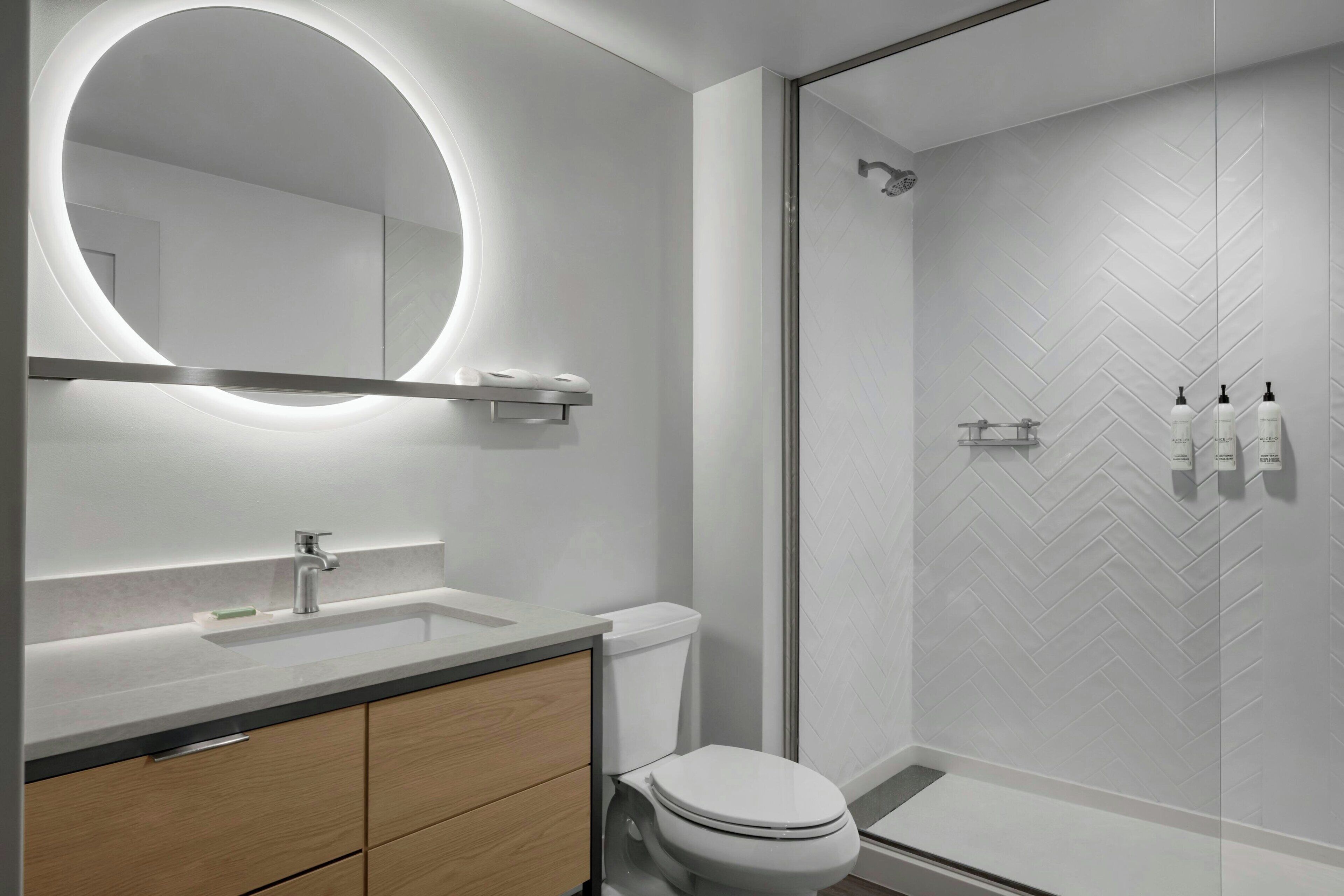 Un baño moderno con un espejo redondo, un inodoro, un lavamanos y una zona de ducha.