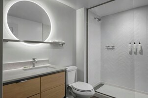 Un baño moderno con un espejo redondo, un inodoro, un lavamanos y una zona de ducha.