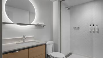 Une salle de bain moderne avec un grand miroir rond, un lavabo, des toilettes et un espace douche.