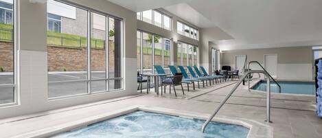 Piscina interna com hidromassagem, espreguiçadeiras e amplas janelas com vista para o exterior.