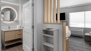 A modern hotel room with a minimalist design, featuring a large window, a flat-screen TV, a built-in bookshelf, and a separate seating area. - Towneplace Suites By Marriott Nampa (Nampa)