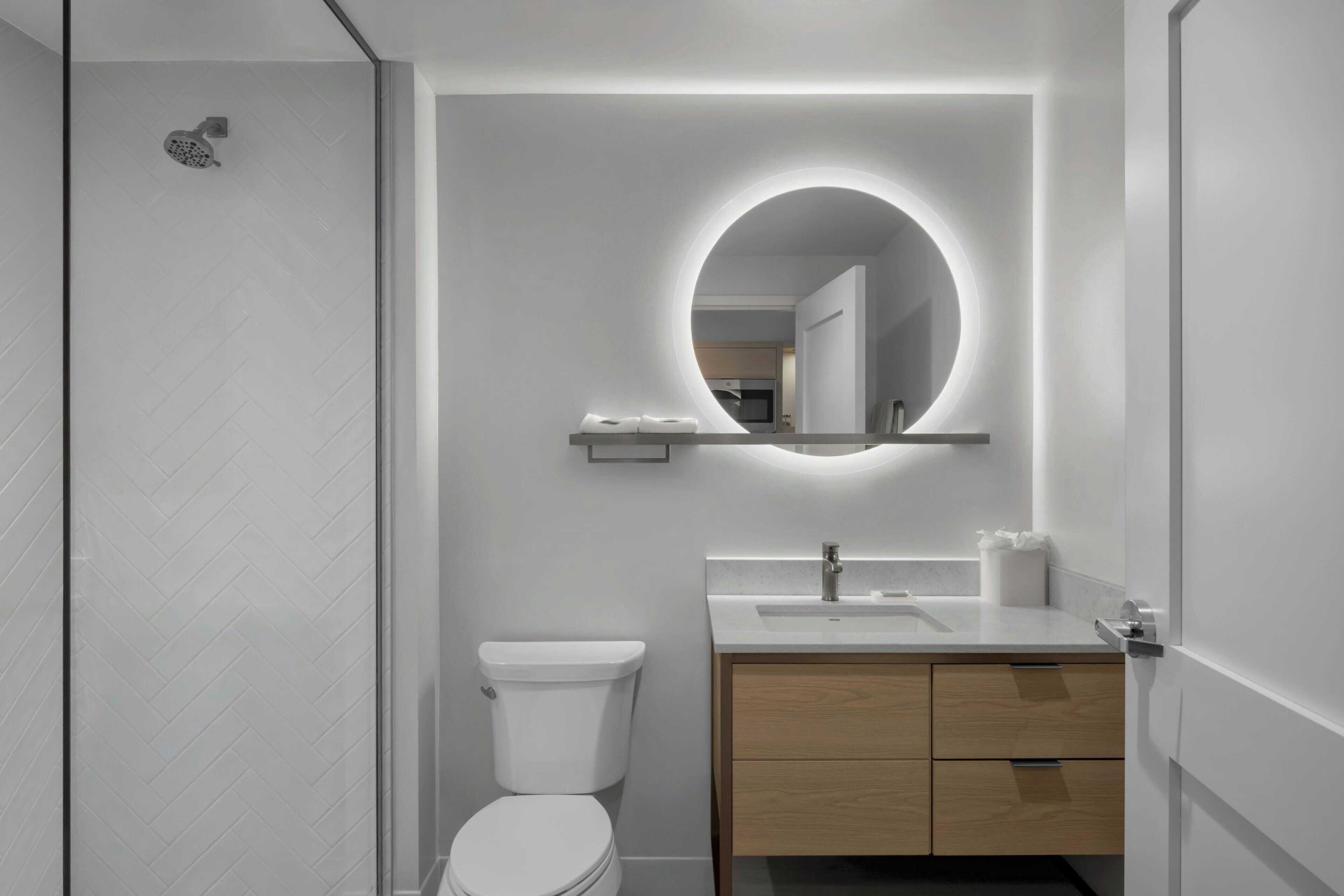 Uma casa de banho moderna com sanita, lavatório e espelho com luz circular.