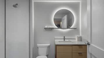 Uma casa de banho moderna com sanita, lavatório e espelho com luz circular.