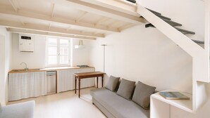 Ein kompakter Wohnbereich mit Küchenzeile, einer Couch, einem Tisch und einer Treppe.