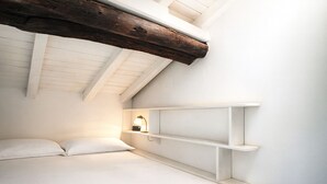 Ein kleines, gemütliches Schlafzimmer mit schrägem Dach, einem Bett und eingebauten Regalen.