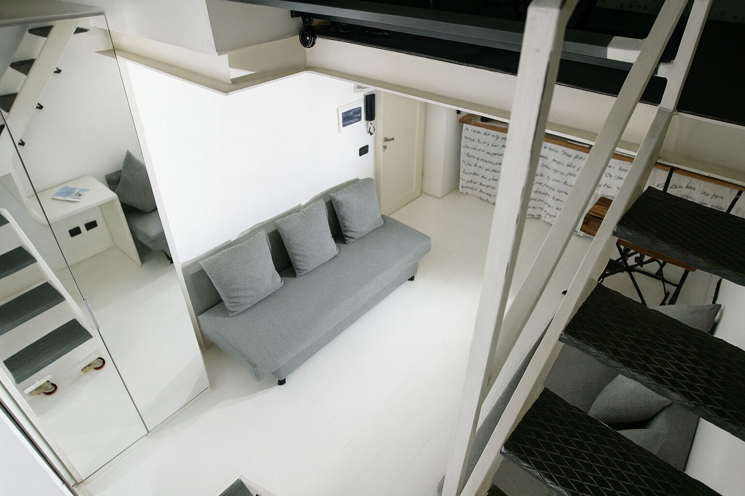 Ein kompakter, moderner Raum mit grauem Sofa, einem kleinen Tisch und einer Treppe.
