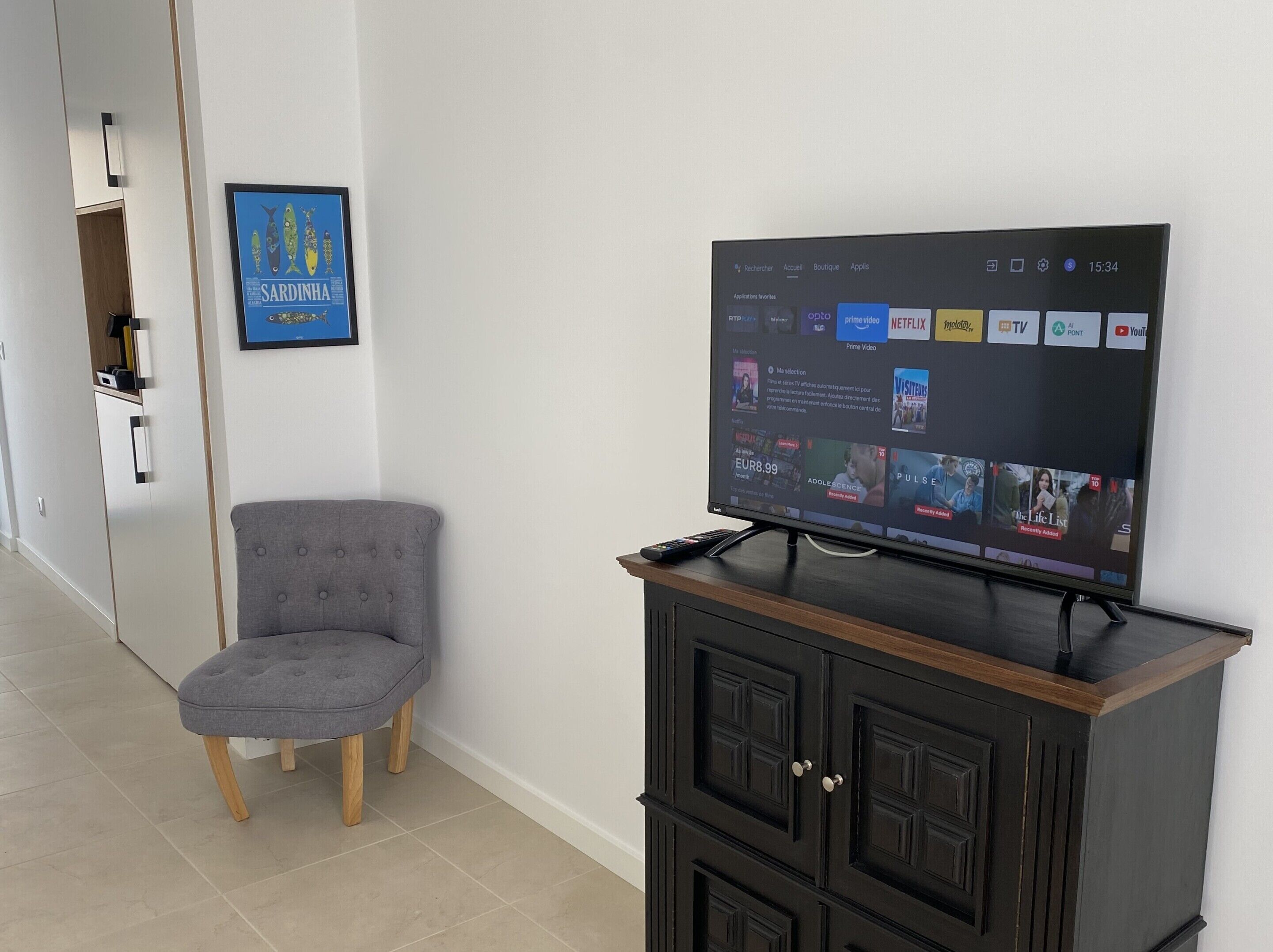 Una sala moderna con un televisor de pantalla plana sobre un mueble de madera, un sillón gris y un cuadro enmarcado de Cerdeña en la pared.