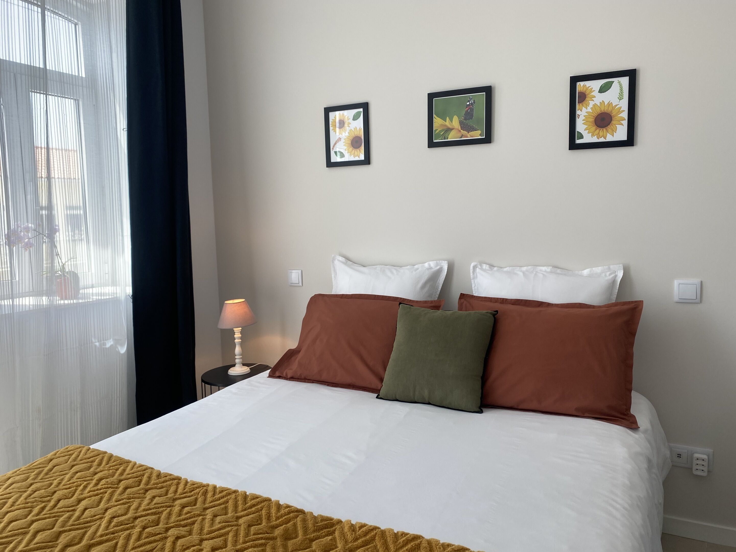 Hotellihuone, jossa on sänky, yöpöytä, lamppu ja kolme kehystettyä kuvaa seinällä.