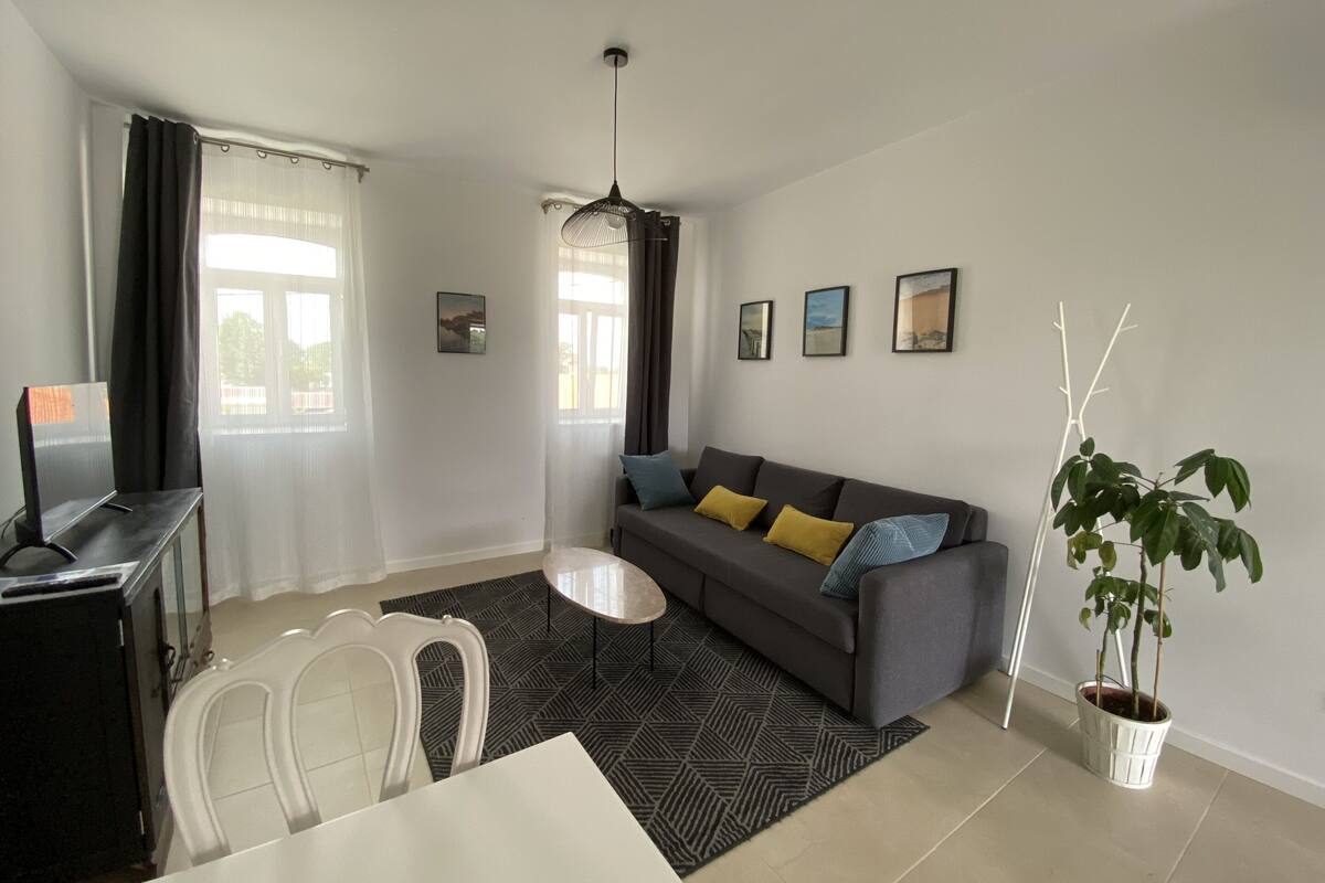 Una sala de estar con sofá, mesa de comedor, sillas, ventilador de techo y una planta en maceta.