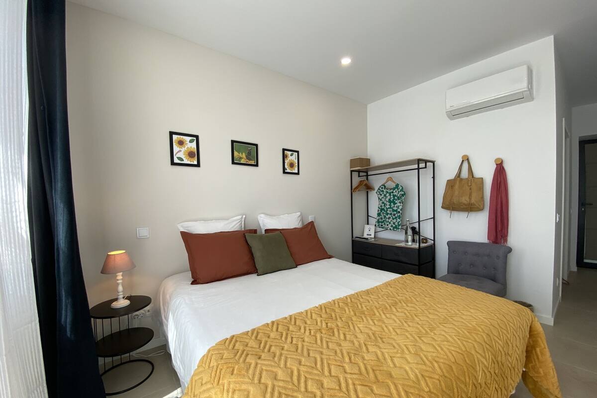 Habitación de hotel con cama, mesita de noche, lámpara, equipo de aire acondicionado y una obra de arte colgada en la pared.