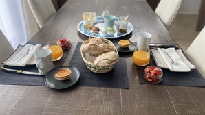 Una tavola imbandita con prodotti per la colazione, tra cui pane, pasticcini e frutta, con vista su una cucina moderna sullo sfondo.