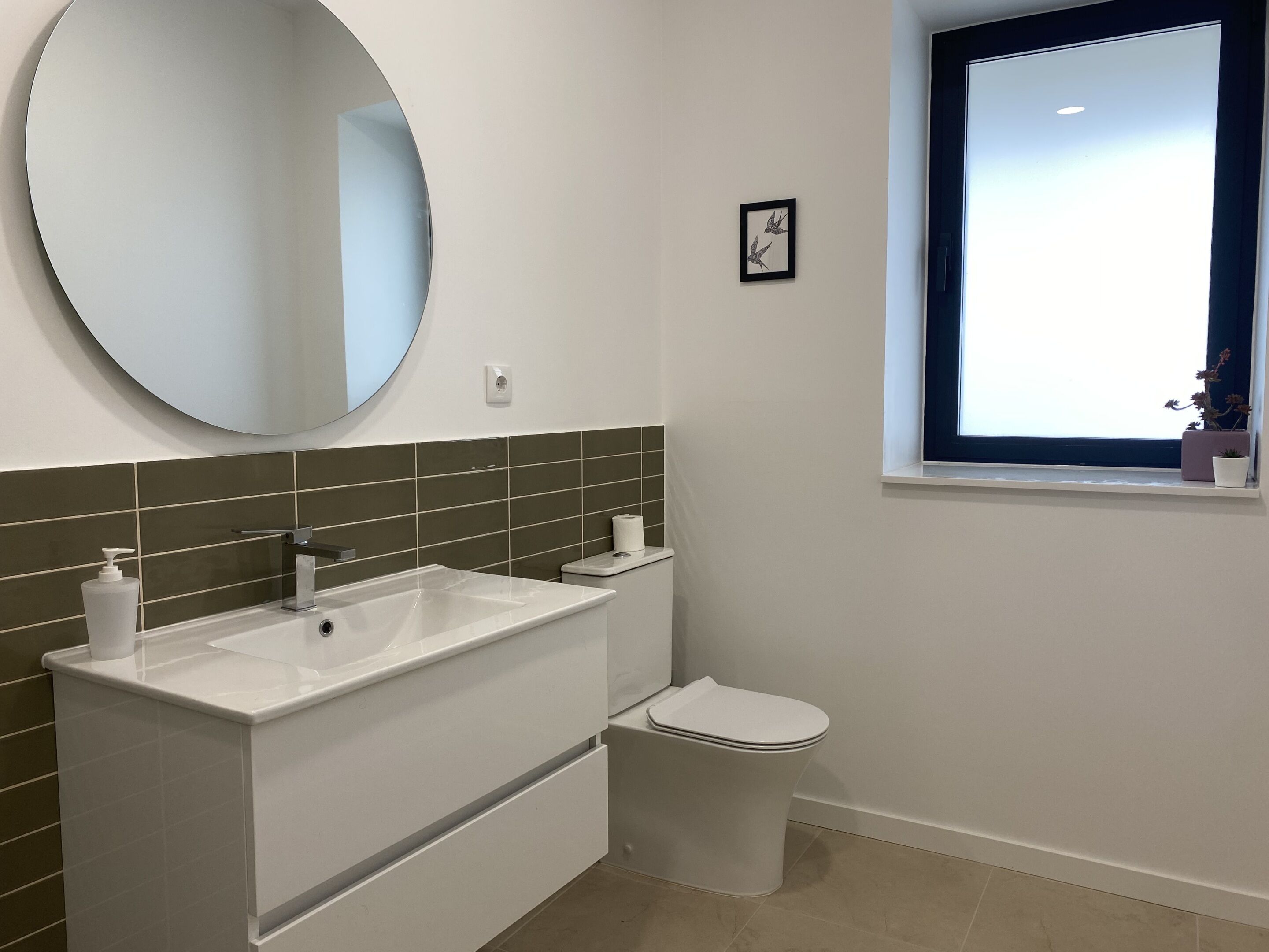 Un baño con un lavamanos blanco, inodoro y ventana con vistas.