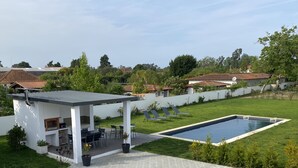 Patio moderno all'aperto con piscina, circondato da un prato curato e un muro bianco.
