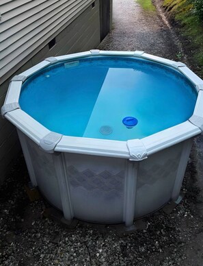 Une piscine hors sol octogonale, avec un intérieur d’un bleu clair, entourée de gravier et avec une maison en arrière-plan.