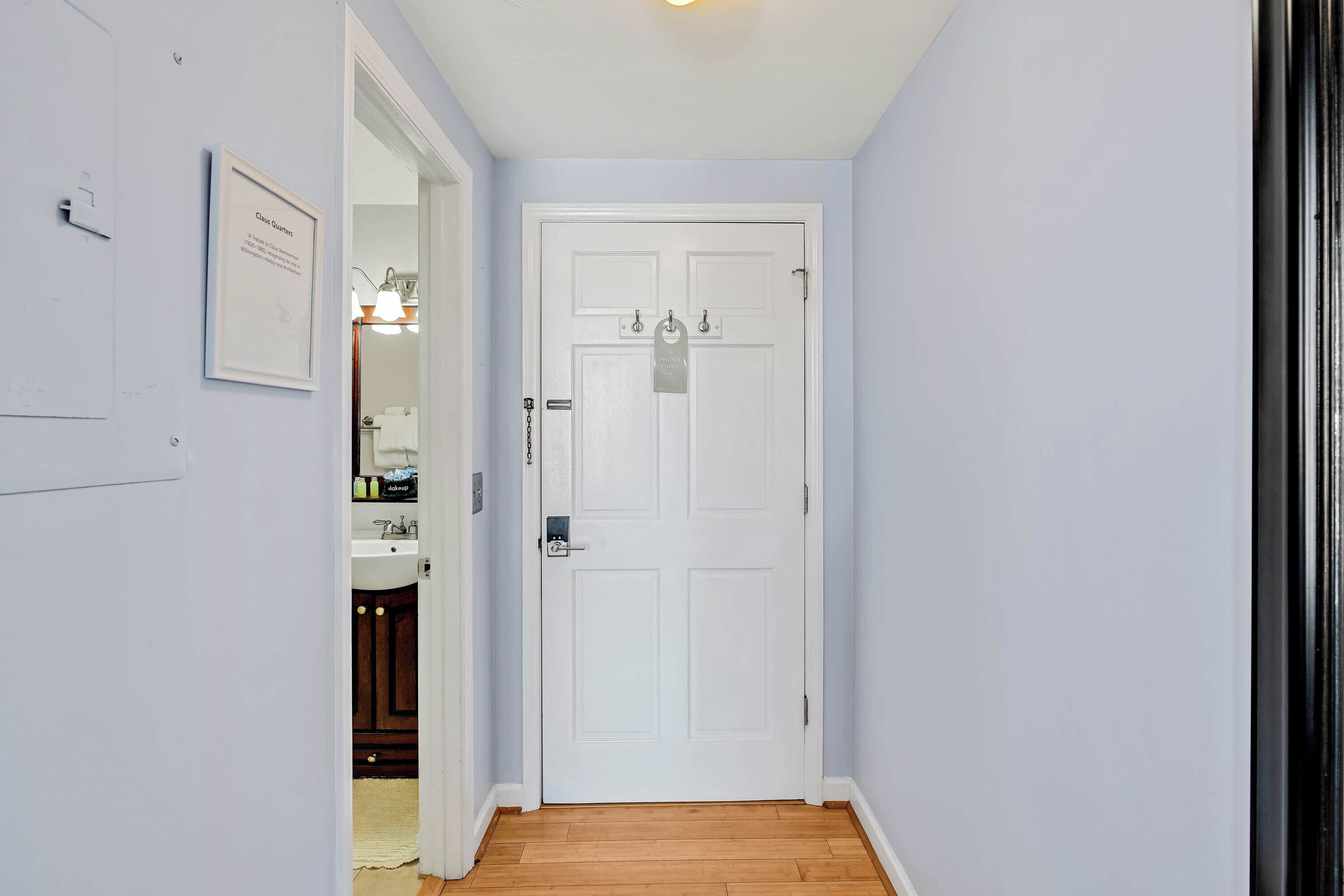 A hallway with a white door, a framed certificate on the wall, and wooden flooring.
