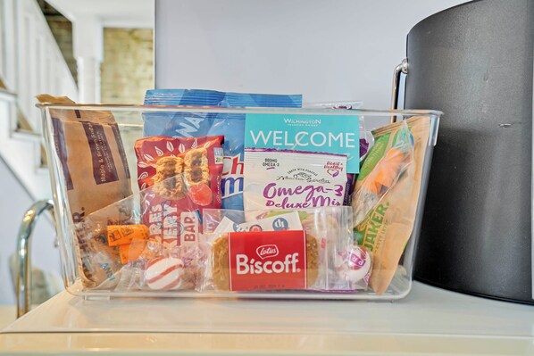 Un récipient transparent en plastique contenant divers en-cas, notamment une carte de bienvenue, un biscuit Biscoff et d’autres collations emballées.