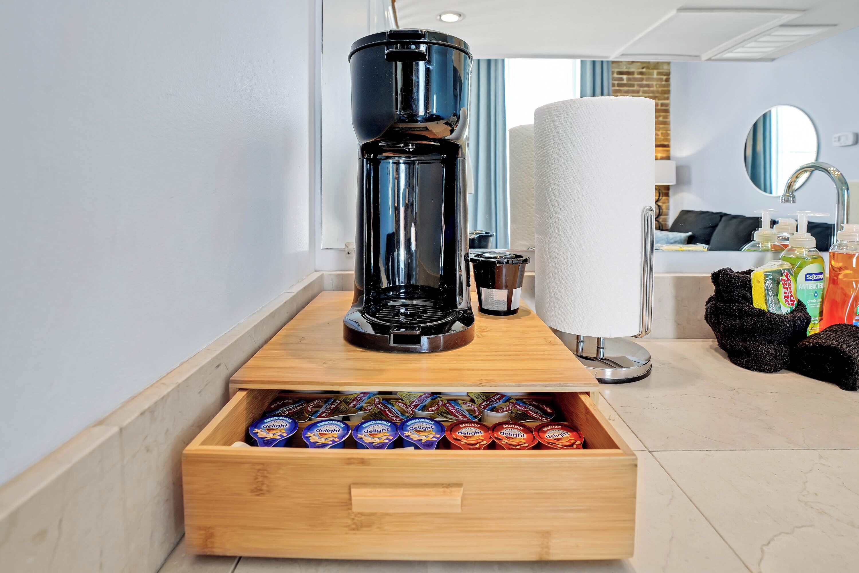 Une machine à café posée sur un plateau en bois, avec un tiroir contenant des en-cas en dessous.