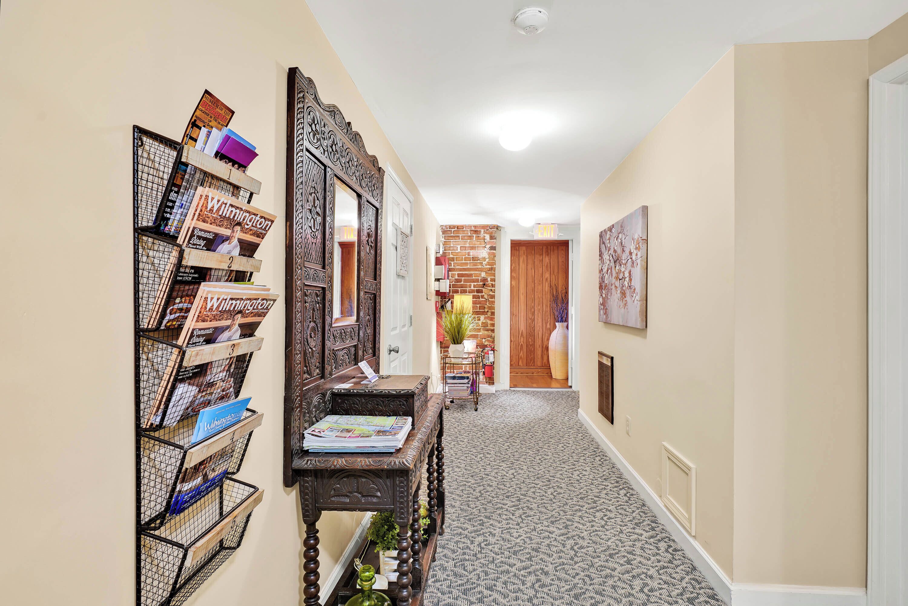 A hallway with a bookshelf, a mirror, and a door leading to another room.