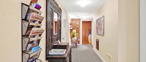 A hallway with a bookshelf, a mirror, and a door leading to another room.