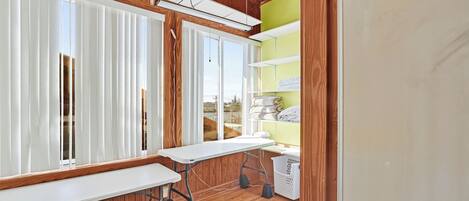 Una habitación con suelo de madera, una mesa blanca y una estantería verde.