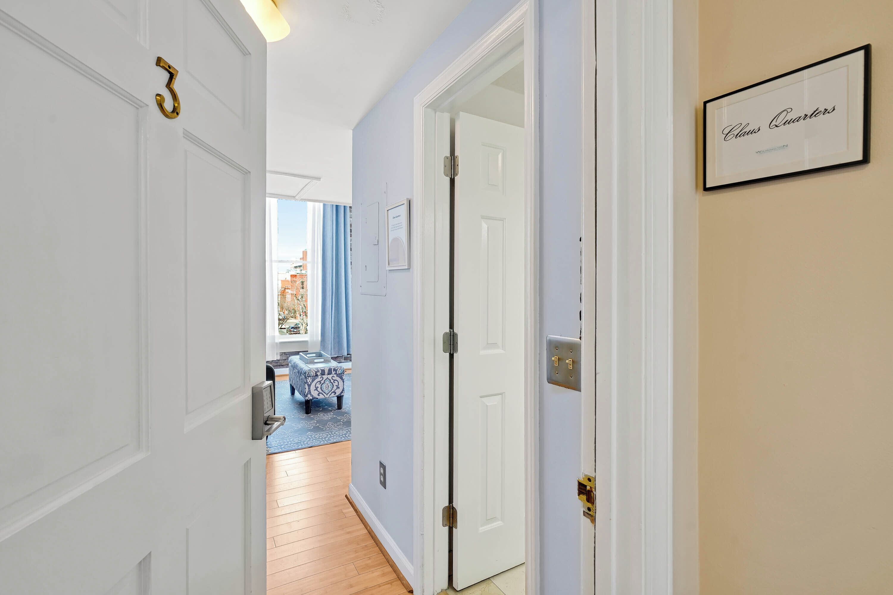 A hallway with a door labeled "Claus Quarters," a blue and white patterned sofa, and a view of the outside.