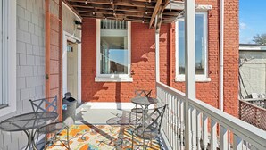 A balcony with a patterned rug, metal chairs, and a white railing. - Claus Quarters on Front! Perfect location in the Heart of Downtown! (wilmington)
