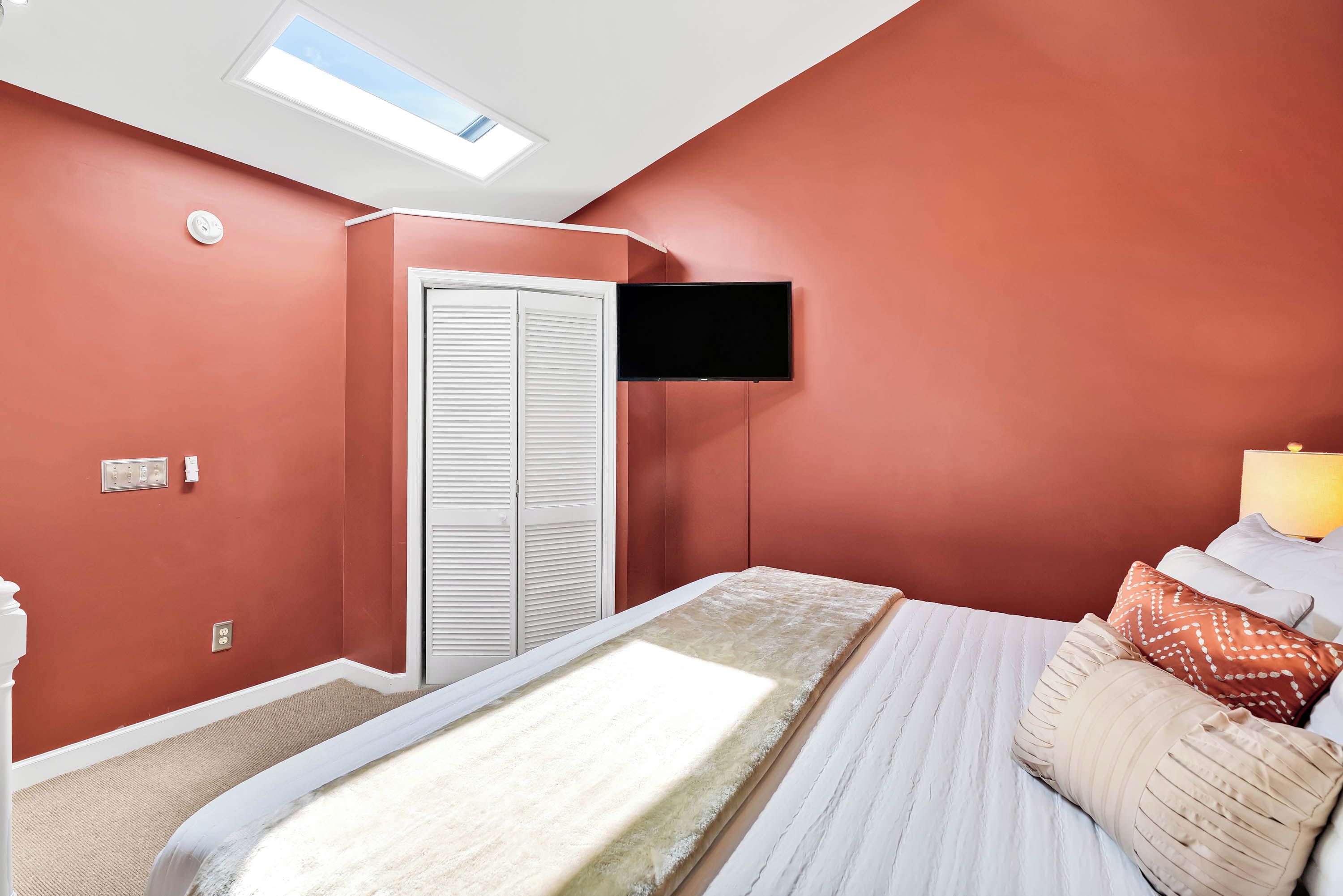 A bedroom with a bed, a TV mounted on the wall, a closet, and a skylight.