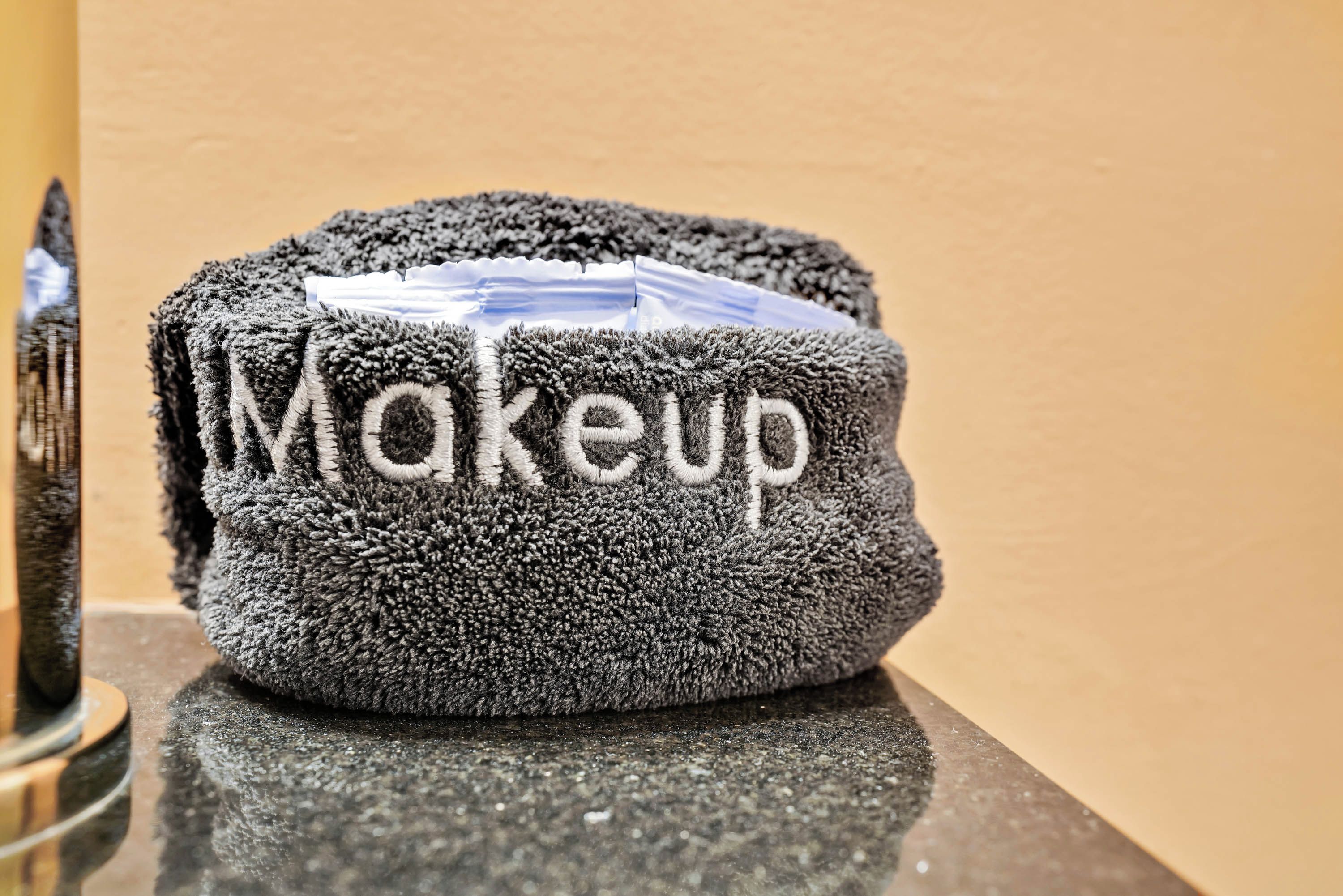 A grey, textured towel with the word "Makeup" embroidered on it, placed on a reflective surface.