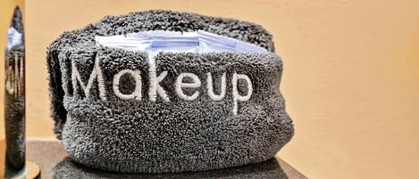 A grey, textured towel with the word "Makeup" embroidered on it, placed on a reflective surface.