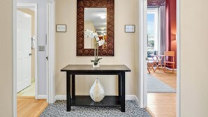 Un couloir avec une console en bois, un miroir décoratif et un vase contenant des fleurs blanches.