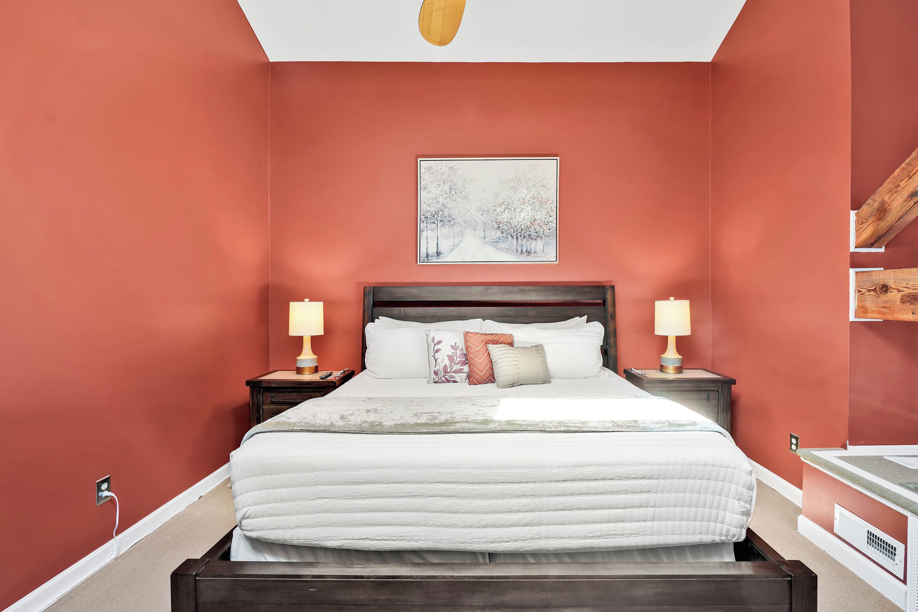 Een slaapkamer met een groot bed, twee nachtkastjes met lampen, een schilderij aan de muur en een houten balk in het plafond.