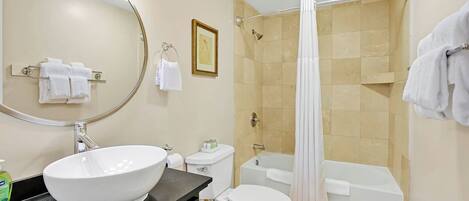 A bathroom with a large mirror, a white sink, a toilet, a bathtub, and a shower curtain.