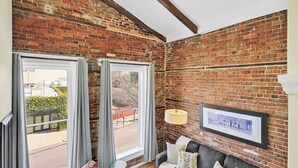 A room with exposed brick walls, a grey sofa with patterned cushions, a small round table, and a floor lamp. - Stemmerman Suite on Front! Perfect location in the Heart of Downtown! (wilmington)