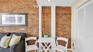 A room with a brick wall, a white table with two chairs, a grey sofa with cushions, and a framed picture on the wall. - Stemmerman Suite on Front! Perfect location in the Heart of Downtown! (wilmington)